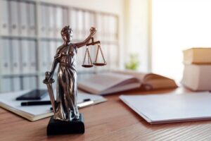 A small statue of Lady Justice is on top of a lawyer's desk. There are legal documents and books around.